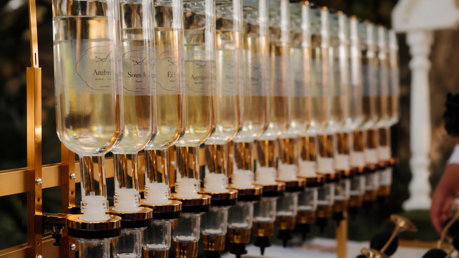 Flacons de parfum personnalisés, présentés tête en bas sur leur distributeur doré, sur fond de verdure.